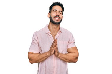 Sakallı, sıradan tişörtlü İspanyol bir adam elleri bağlı yalvarıyor ve dua ediyor. Yüzünde umut ifadesi var. Çok duygusal ve endişeli. Yalvarıyor. 