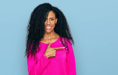 Orta yaşlı Afro-Amerikalı kadın, günlük kıyafetler giyiyor, neşeli, yüzünde mutlu ve doğal bir ifadeyle, elleri ve parmaklarıyla yüzünü gösteren bir gülümseme var. 