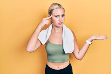 Spor giyimli, havluyla kafası karışmış ve avuç içi açık bir şekilde fotokopi alanını gösteren ve alnını işaret eden genç sarışın bir kız. Bunu bir düşün.. 