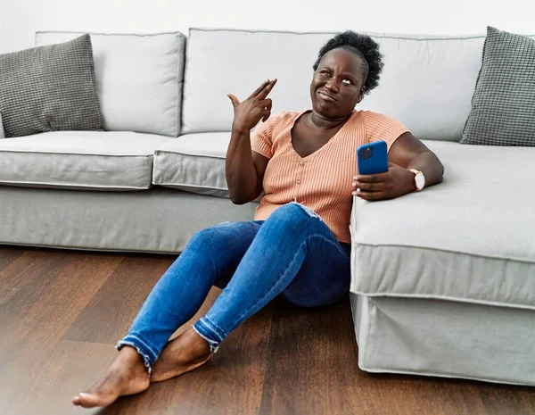 年轻的非洲女人用智能手机坐在家里的地板上 用枪指着自己的头开枪自杀 — 图库照片