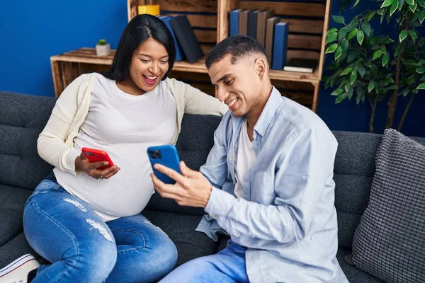 Young Latin Couple Expecting Baby Using Smartphone Sitting Sofa Home — Foto Stock