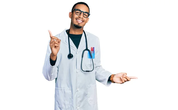 医師の制服を着た若いアフリカ系アメリカ人の男性と聴診器は 異なる方向に指で自信を持って指して笑顔 広告のコピースペース — ストック写真