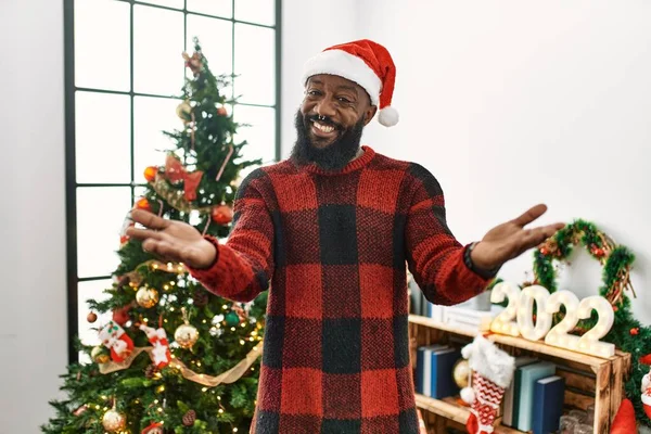 アフリカ系アメリカ人男性身に着けているサンタクラスの帽子立っているクリスマスツリー笑顔明るい提供手支援と受け入れ — ストック写真
