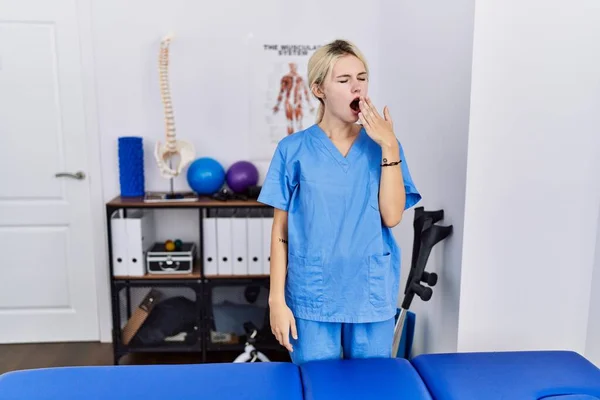 Jovem Fisioterapeuta Mulher Trabalhando Clínica Recuperação Dor Entediado Bocejo Cansado — Fotografia de Stock