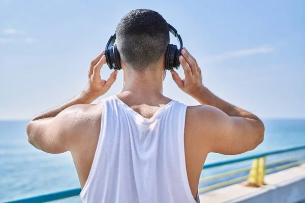 ヘッドフォンを身に着けているヒスパニック系のスポーツマンは晴れた日に海で音楽を聴く — ストック写真