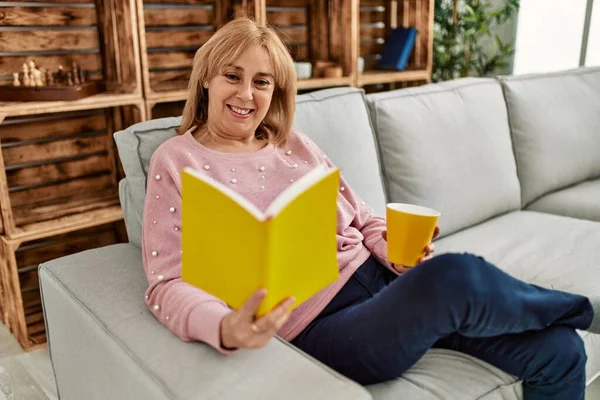 Orta Yaşlı Sarışın Kadın Gülümsüyor Mutlu Kitap Okuyor Evde Kahve — Stok fotoğraf