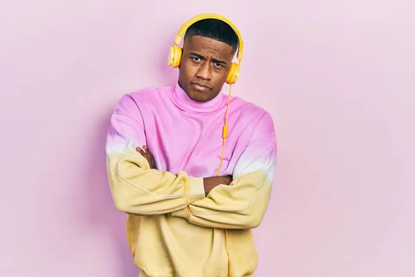 Young black man listening to music wearing headphones skeptic and nervous, disapproving expression on face with crossed arms. negative person.