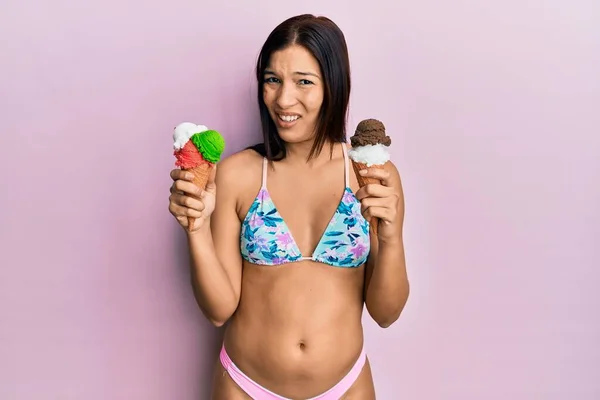 ビキニ姿の若いラテン系の女性は アイスクリームを持っていないと混乱した表情 疑わしい概念 — ストック写真