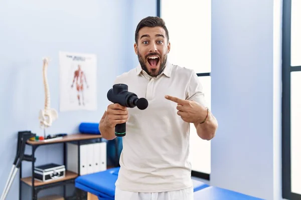 Schöner Hispanischer Mann Mit Therapie Massagepistole Physiotherapiezentrum Lächelt Glücklich Und — Stockfoto