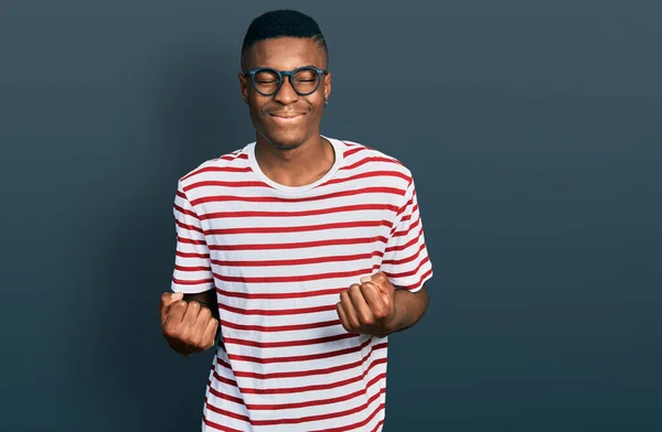 若いアフリカ系アメリカ人の男性は シャツや眼鏡を着用非常に満足し 腕を上げて勝者のジェスチャーを行う興奮し 笑顔と成功のために叫んで お祝いのコンセプト — ストック写真