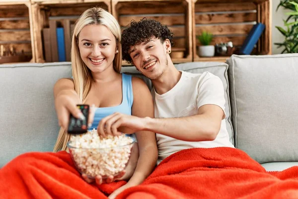 Young couple watching film and eating popcorn sitting on the sofa at home.