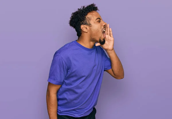 ひげを生やした若いアフリカ系アメリカ人の男性は カジュアルな紫色のTシャツを着て大声で叫び 口の上で手で横に叫んでいます コミュニケーションの概念 — ストック写真