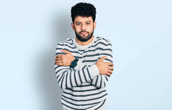 Young arab man with beard wearing casual striped sweater shaking and freezing for winter cold with sad and shock expression on face