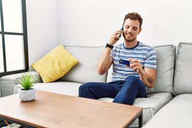 Genç İspanyol adam elinde kredi kartıyla akıllı telefondan konuşuyor.
