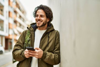 Duvara dayanmış akıllı telefon kullanan yakışıklı İspanyol.