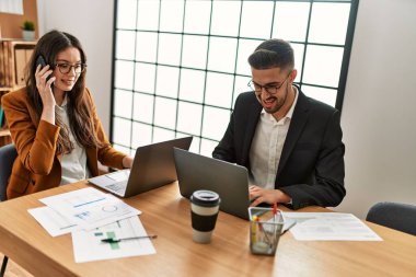 Ofiste akıllı telefon ve dizüstü bilgisayar kullanarak çalışan iki İspanyol iş adamı..