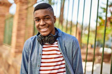 Genç Afrikalı Amerikalı adam şehirde kulaklık takarak mutlu bir şekilde gülümsüyor..