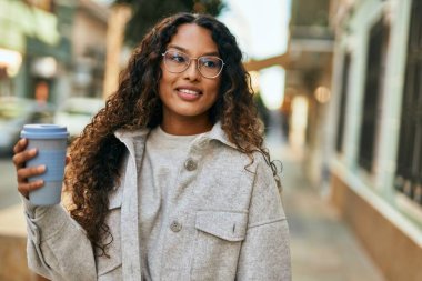 Genç Latin kadın gülümsüyor, şehirde kahve içiyor..