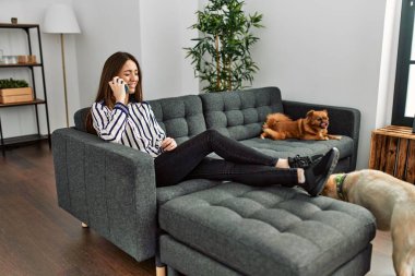 Genç İspanyol kadın akıllı telefonda konuşuyor. Kanepede oturuyor, evde köpeklerle.