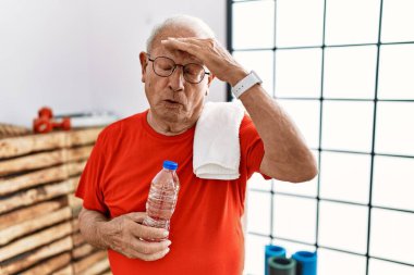 Spor kıyafetleri ve havluyla spor salonunda oturan son sınıf öğrencisi, alnında bir sorun olduğu için endişeli ve stresli. Kriz için endişeli. 