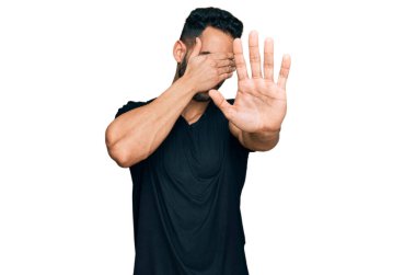 Sakallı, sıradan siyah tişörtlü, elleriyle gözlerini kapatan, üzgün ve korku ifadeli İspanyol bir adam. utangaç ve olumsuz kavram. 