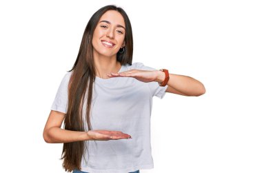Latin kökenli genç bir kız, günlük beyaz tişörtler giyiyordu. Elleri büyük ve büyük bir işaret gösteriyordu. Ölçü sembolü. Kameraya bakıp gülümsüyor. ölçüm kavramı. 