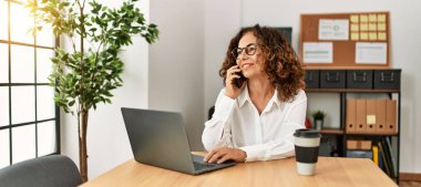 Ofiste çalışan orta yaşlı İspanyol kadın akıllı telefondan konuşuyor.