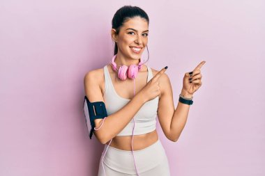 Spor kıyafetleri giyen, kulaklık takan, gülümseyen ve kameraya bakan genç İspanyol bir kadın.. 