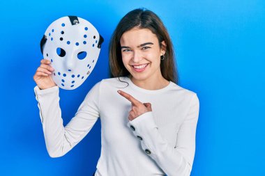 Hokey maskesi tutan genç beyaz kız mutlu bir şekilde elini ve parmağını gösterdi. 