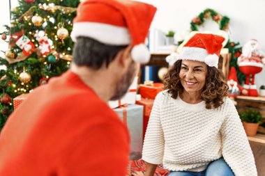 Orta yaşlı İspanyol çift Noel şapkası takıp evde yerde oturuyor..