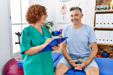 Orta yaşlı erkek ve kadın fizyoterapi üniforması giyip fizik tedavi kliniğinde rehabilitasyon seansı yapıyorlar.