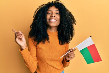 Afro saçlı Afro-Amerikalı kadın elinde madagaskar bayrağı tutarken mutlu bir şekilde gülümsüyor. 