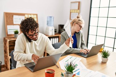 İki iş adamı akıllı telefondan konuşuyor ve ofiste dizüstü bilgisayar kullanıyorlar..