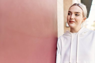 Modern beyaz saç stili ile genç ve güzel bir kadın mutlu bir şekilde dışarıda duvara yaslanıyor.