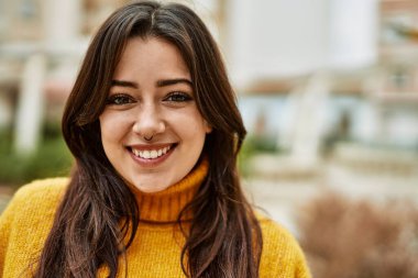 Balıkçı yaka kazak giyen genç, güzel esmer kadın dışarıda mutlu bir şekilde gülümsüyor.