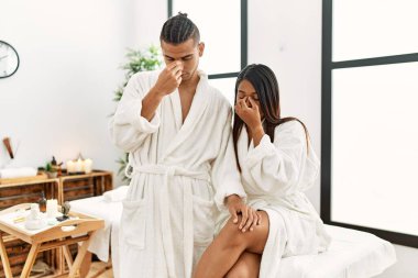 Güzellik merkezinde havluyla dikilen genç latin çift yorgun burunlarını ve gözlerini ovuşturup yorgunluk ve baş ağrısı hissediyorlar. Stres ve hüsran kavramı. 