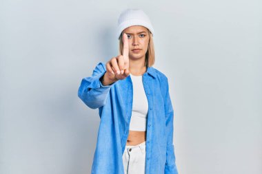 Yün şapka takan güzel sarışın kadın parmağını kaldırmış ve kızgın bir ifade takınıyor. Hiç hareket göstermiyor. 