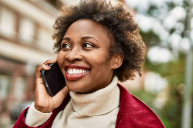 Güzel iş kadını afro saçlı Afro-Amerikan kadın mutlu ve kendinden emin bir şekilde şehirde telefonda konuşuyor.
