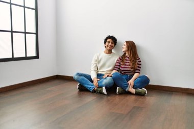 Genç İspanyol çift mutlu bir şekilde gülümsüyor ve boş bir evde yerde oturuyor..