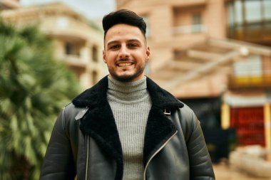 Genç Arap adam gülümsüyor, mutlu bir şekilde şehirde duruyor..