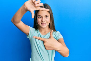 Güzel, esmer, beyaz tişört giyen, gülümseyen, elleri ve parmakları mutlu yüzlü küçük bir kız. yaratıcılık ve fotoğrafçılık kavramı. 