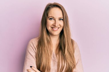 Kollarını kavuşturup kameraya bakarak gülümseyen gündelik süveter giyen genç sarışın kadın. pozitif kişi. 