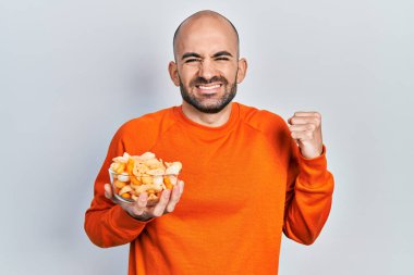 Patates cipsi tutan genç kel adam gururla bağırıyor, zaferi kutluyor ve başarıyı kollarını kaldırarak kutluyor. 