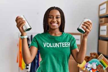 Gönüllü üniforma giyen genç Afrikalı Amerikalı kadın yardım merkezinde konserve yiyecek tutuyor.