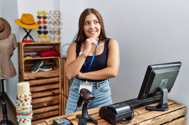 Perakende dükkanında eli çenesinde açık afiş taşıyan genç esmer kadın soru sormayı, düşünceli ifadeyi düşünüyor. Gülümseyen ve düşünceli bir yüz. şüphe kavramı. 