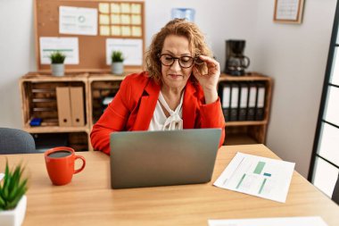 Ofiste çalışan orta yaşlı beyaz iş kadını dizüstü bilgisayar kullanıyor..