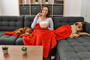 Genç İspanyol kadın evde köpeklerle kanepede oturup film izliyor.