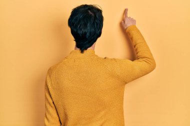 Yakışıklı hippi genç adam gündelik sarı süveter giyip geriye doğru parmak eliyle öne bakıyor. 