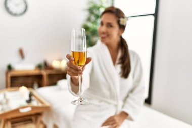 Bornoz giymiş, şampanya içen genç Latin kadın. 