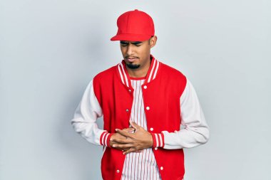 Genç Afro-Amerikan adam beyzbol üniforması giyiyor ve midesi üstünde çünkü hazımsızlık, acı verici bir hastalık kendini iyi hissetmiyor. Ağrı kavramı. 